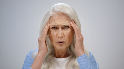 stressed woman having headache indoor. senior lady suffering from pain inside.