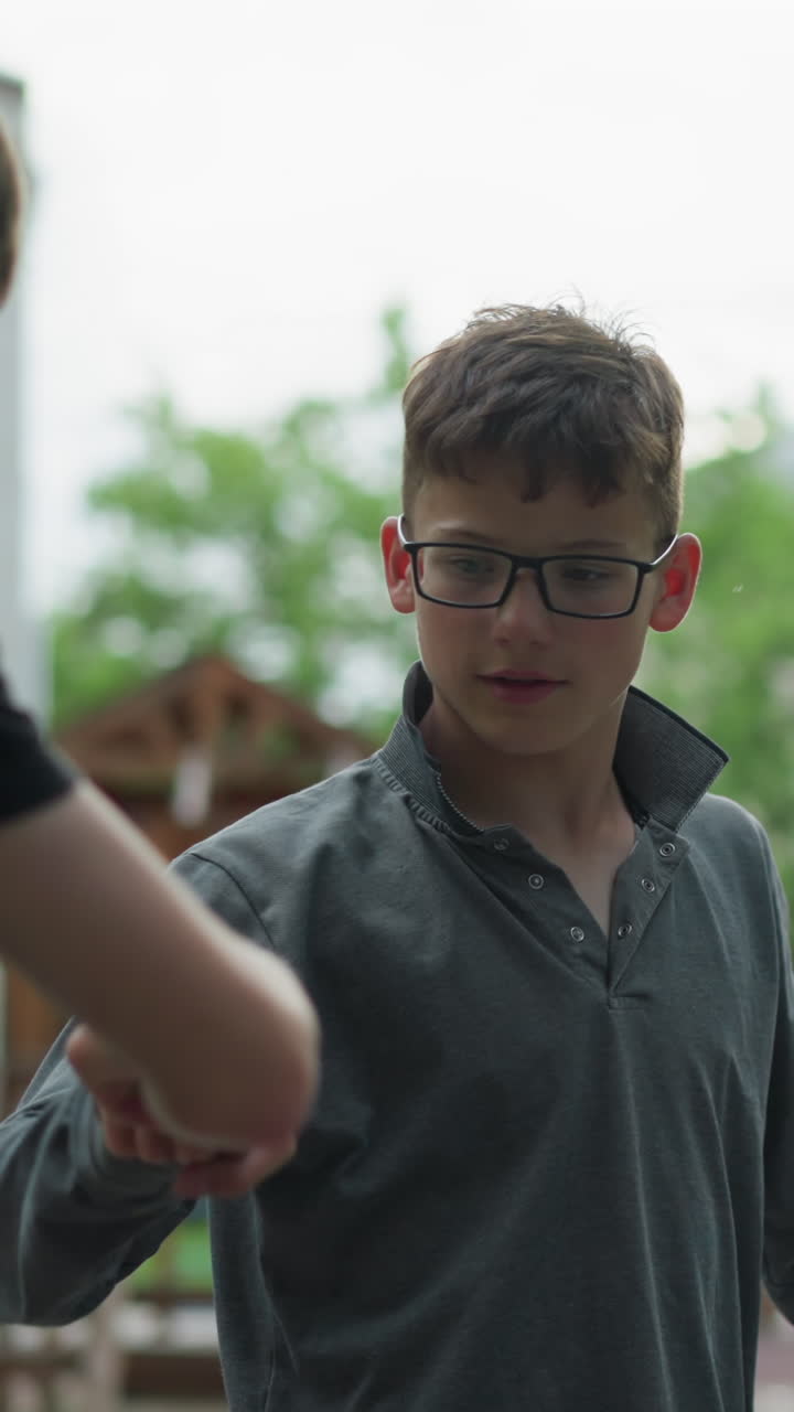 dos hermanos en bicicletas interactúan lúdicamente, un hermano en una camiseta gris se extiende para cortar los nudillos de las manos con el otro, ambos sonriendo en un momento alegre, con el fondo borroso de la construcción