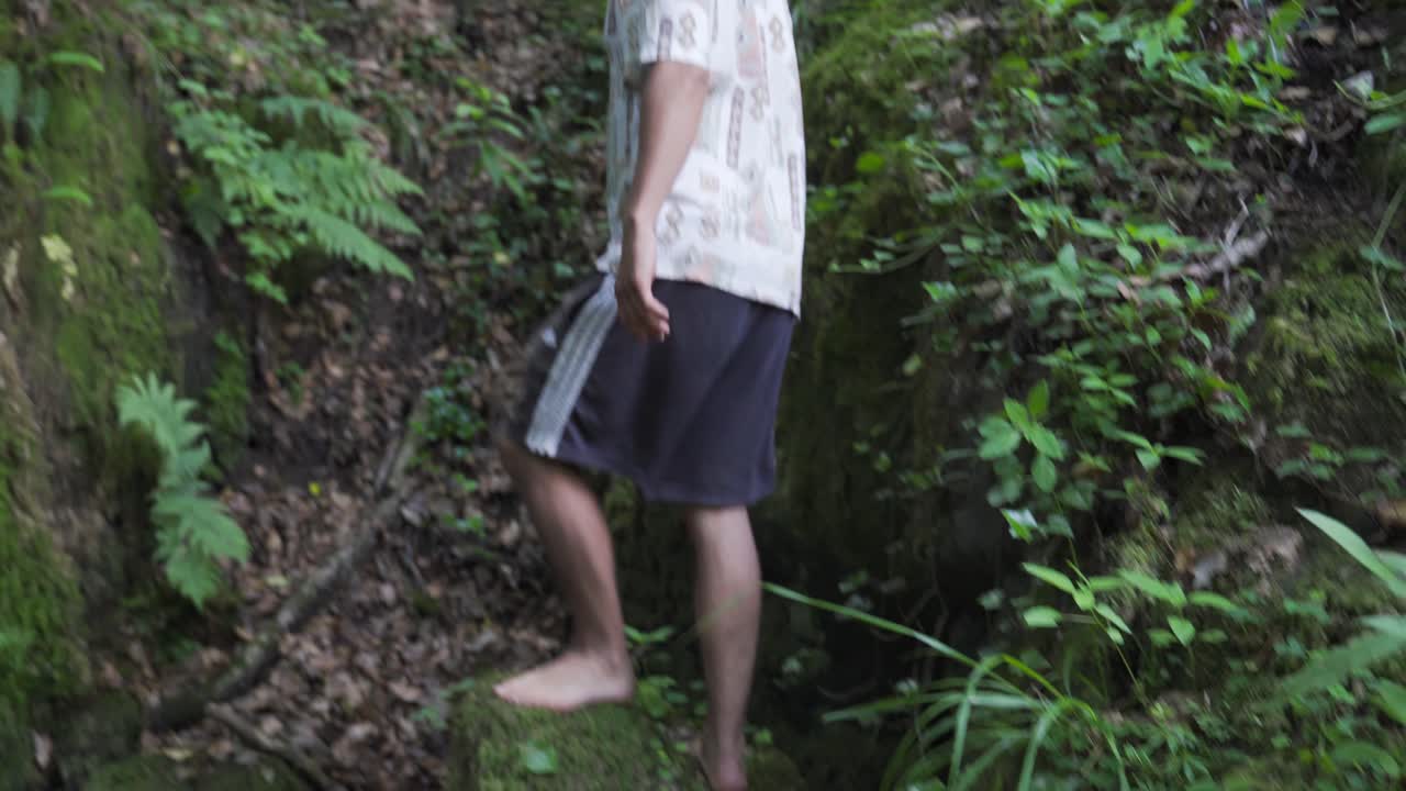 젊은 남자는 포레스트의 아름다운 야생 폭포에서 돌 위를 걷고 카메라와 줌 렌즈로 사진을 찍습니다