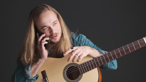 caucasian young man having a call while holding guitar.