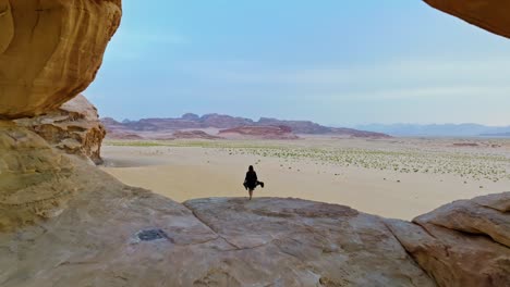 Pullback-Reveal-Of-A-Woman-Standing-At-Kharaza-Arch-Overlooking-Desert-In-Wadi-Rum,-Jordan