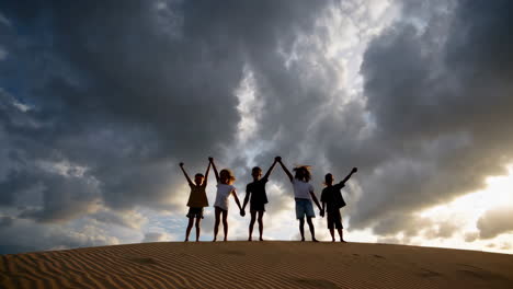children celebrate on a sand dune at sunset