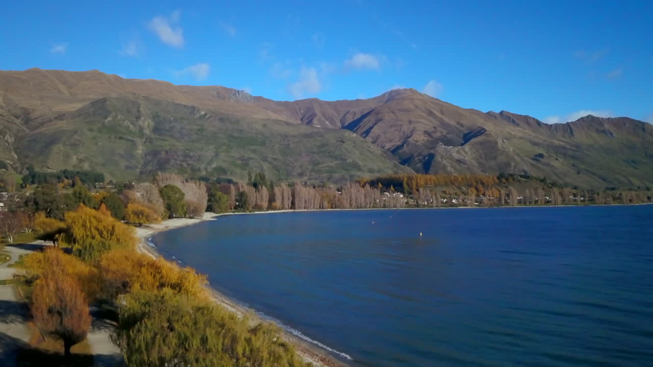 la costa del lago wanaka nueva zelandia verano otoño otoño avión no tripulado cinematográfico asombroso cielo azul hermosa mañana tarde cardrona queenstown isla sur pareja caminando lentamente hacia abajo movimiento