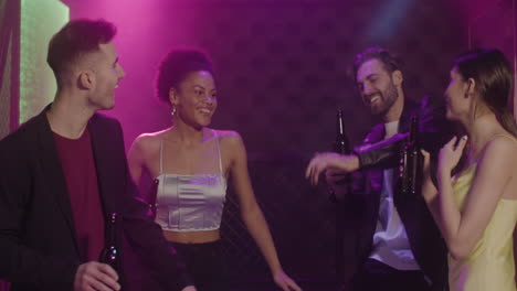 group of four young friends holding beer and dancing at disco 1