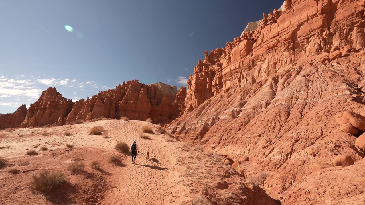 Donna e il suo cane al guinzaglio che camminano sotto le suggestive scogliere di arenaria nel Goblin Valley State Park, Utah USA