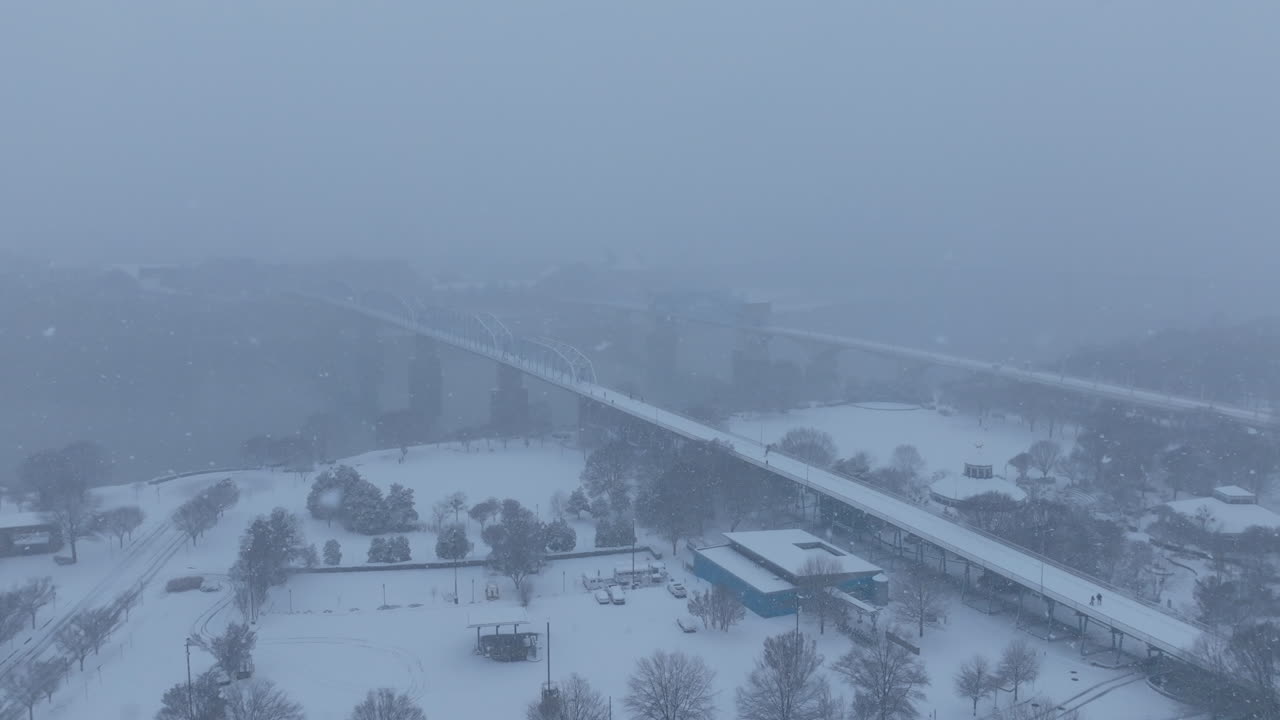 Aerial footage flying over Coolidge Park with the Walnut Street Walking Bridge in the background during a snowstorm in Chattanooga, TN.