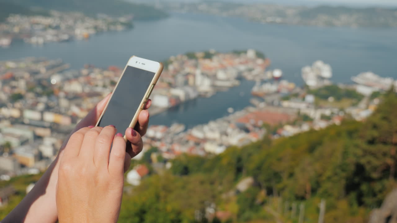 manos femeninas con un teléfono inteligente usan el teléfono contra el fondo de la ciudad de bergen video 4k