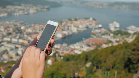 manos femeninas con un teléfono inteligente usan el teléfono contra el fondo de la ciudad de bergen video 4k