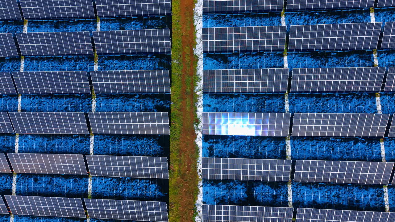 Vista dall'alto simmetrica di file di pannelli solari blu. Ripresa aerea ravvicinata di un impianto fotovoltaico con un sentiero sterrato centrale. Motivo geometrico di moduli per energia pulita.