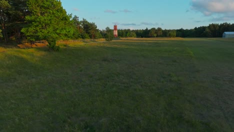 flying over a field towards a soviet style lighthouse in the countryside, evening light