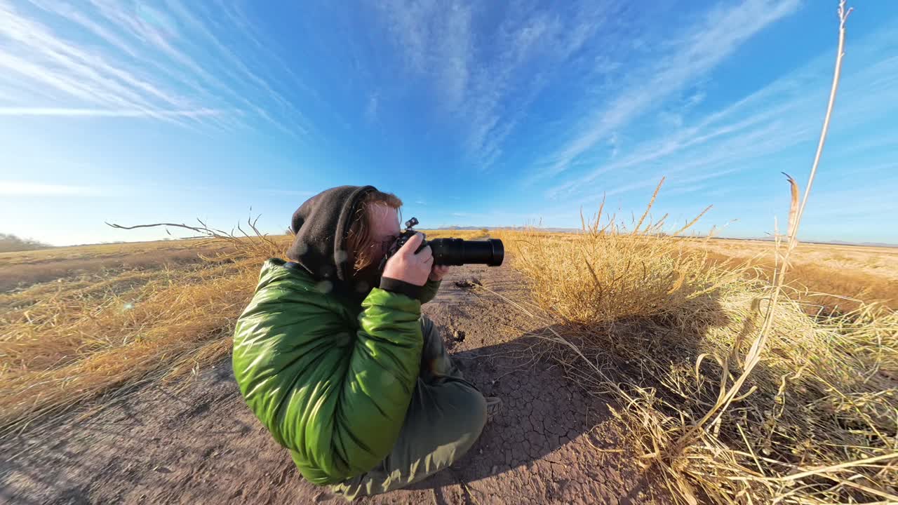 Red hair male photographer in Arizona grasslands filming birds.