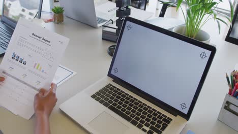 Hands-of-businesswoman-reading-report-and-using-laptop-at-desk-in-office,-copy-space-on-screen