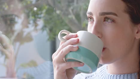 Thoughtful-caucasian-woman-drinking-coffee-at-window-in-slow-motion