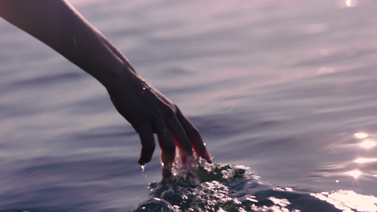 가까운 여성의 손이 물의 물결을 만지고 관광객이 보트 타기를 즐기고 있습니다.