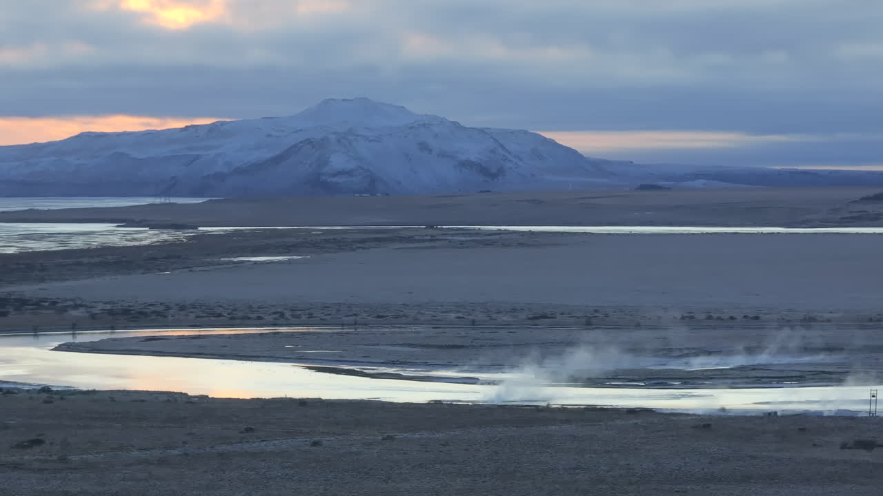 Damp stiger op fra Laugaras Lagune på Island, geotermisk aktivitet med sneklædte bjerge i baggrunden, luftfoto