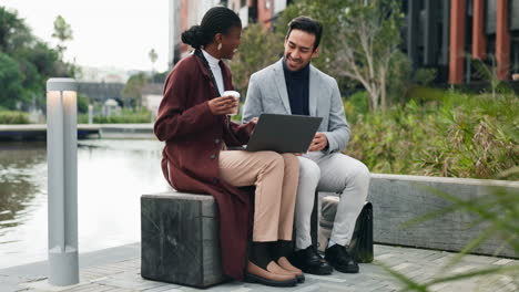 two business colleagues have a coffee break outdoors and look at a laptop.