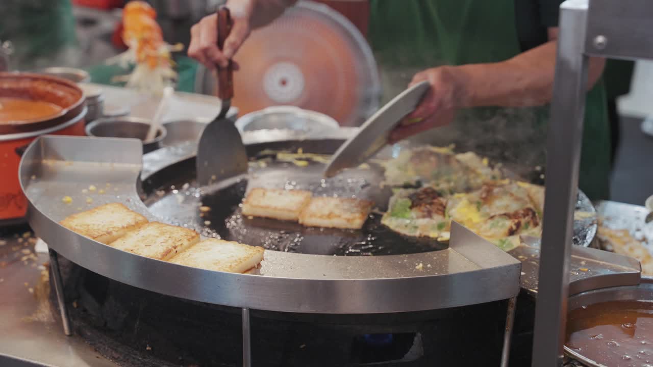 A street vendor frying and flipping sizzling Taiwanese oyster omelette on a hot round griddle, with eggs, oysters, and batter bubbling together into a savory street food delicacy