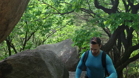 Man-hiker-with-trekking-poles-walking-by-huge-rocks-in-a-mountain-forest---middle-shot