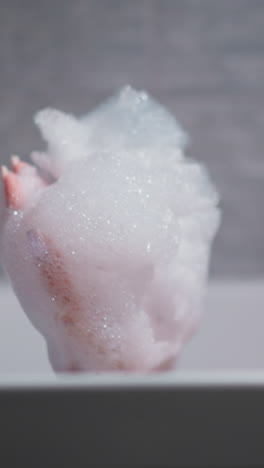 woman blows foam lying in bathtub at home. pleasured lady with soap bubbles on palms rests in bathroom. woman plays with shampoo froth in washroom