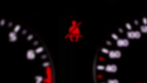 intentionally blurred clip of a blinking flashing seatbelt warning icon, at the center of a modern car's dashboard, big and near