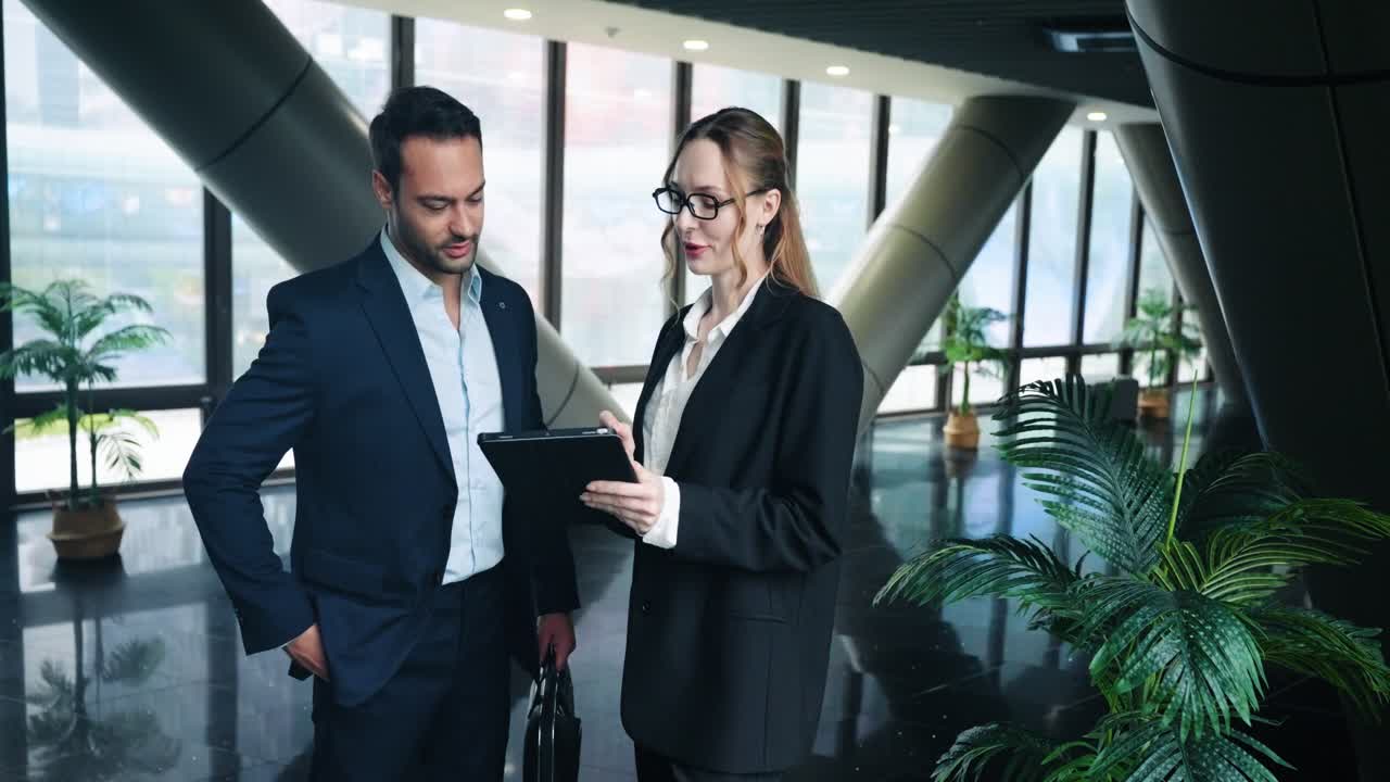 Two Business Professionals Stand And Discuss Work In The Office Hallway. - medium shot