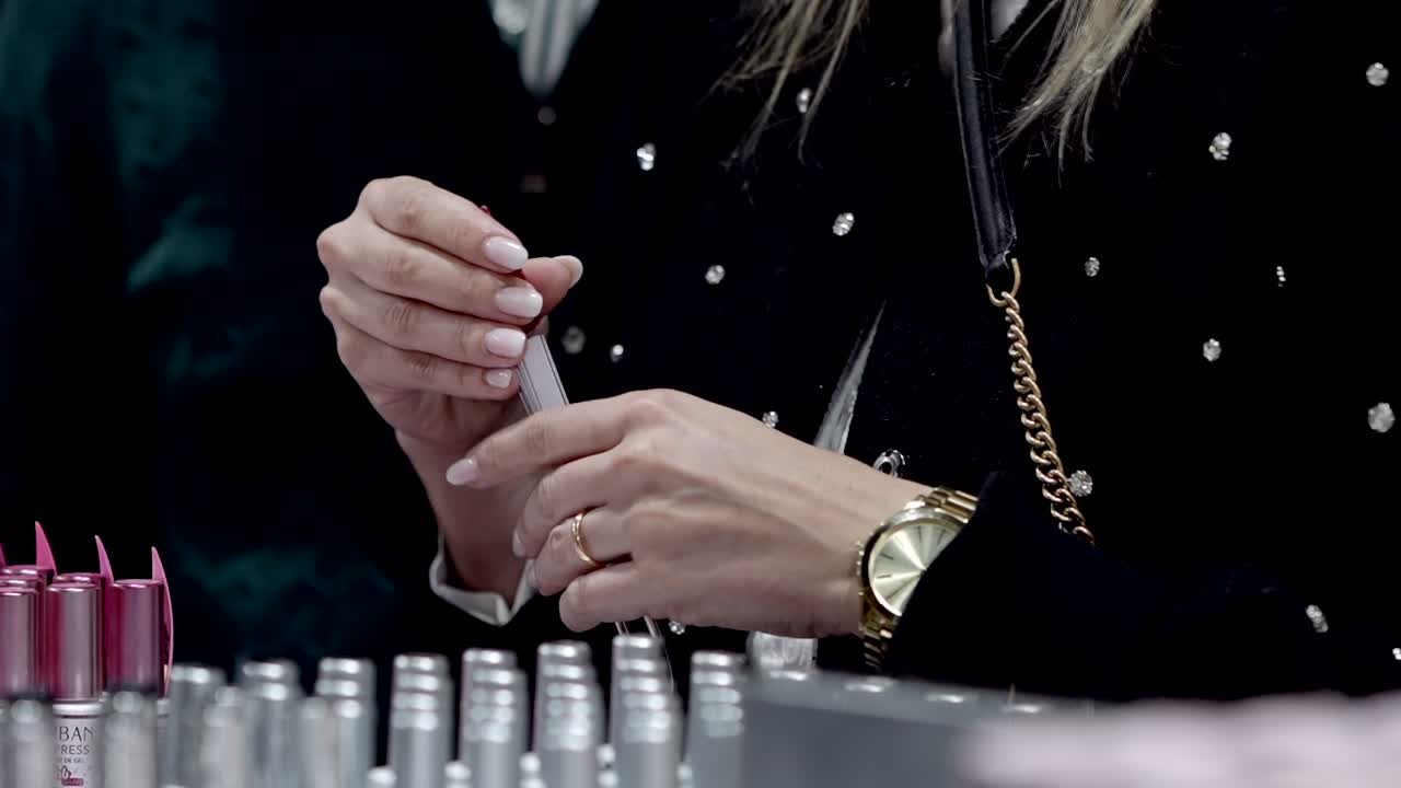 close up of woman holding pink nail polish bottle while browsing cosmetic store display