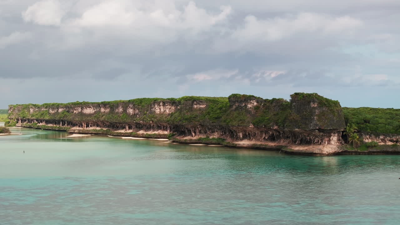 Drone aerial of Lekini Bay, Ouvéa, where steep limestone cliffs tower above turquoise lagoon waters and coral reef formations along the tropical coast