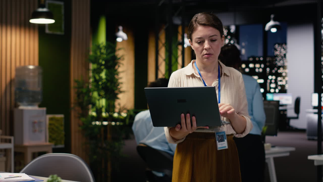 Standing in office at night, woman entrepreneur uses laptop, profitability