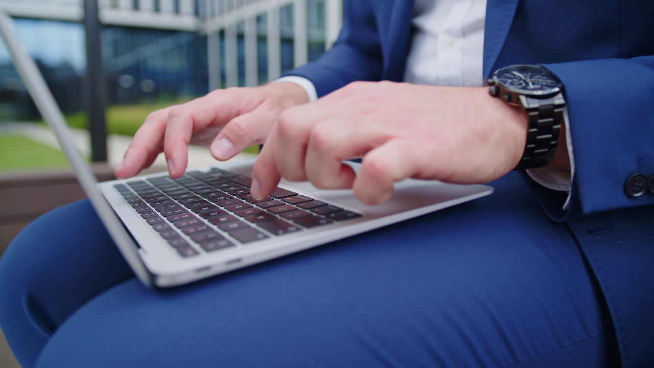 Close-up of suited business man&rsquo;s hands using laptop in lap outdoors