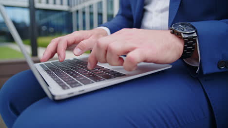 close-up of suited business man’s hands using laptop in lap outdoors