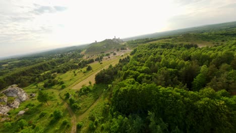 vista aérea de drones fpv de los restos del castillo prehistórico de olsztyn y senderos rodeados de naturaleza y árboles con la vista del paisaje urbano en el fondo, polonia
