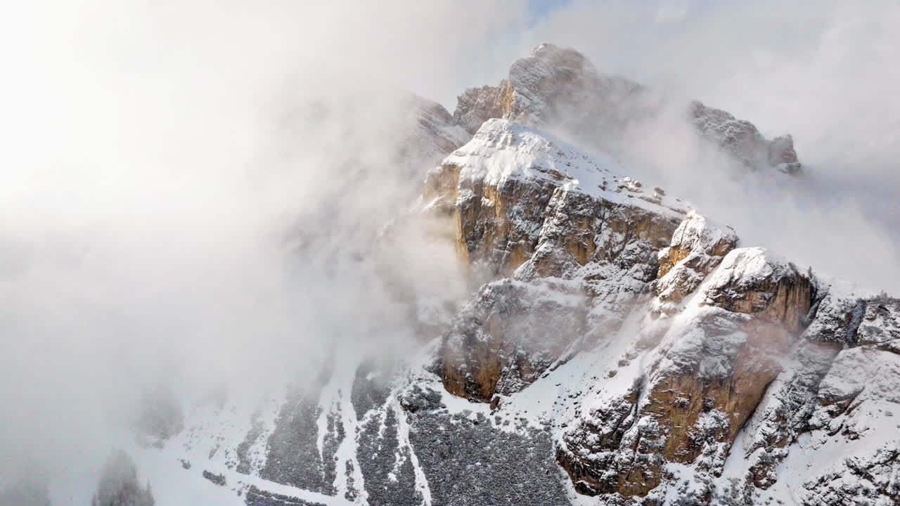 Aerial drone view of snow on the Sassongher mountain in the clouds, in the Dolomites, Italy