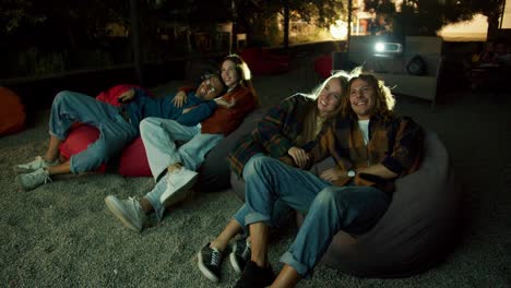 two couples in love are sitting on beanbag chairs and watching a movie. a party outside the city. rest in the country house at the weekend