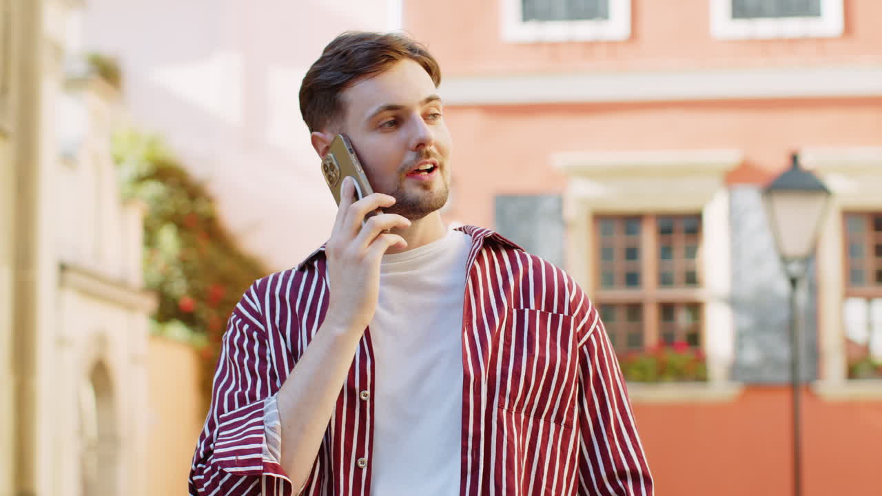 Happy handsome man having remote conversation talking on smartphone good news gossip in city street