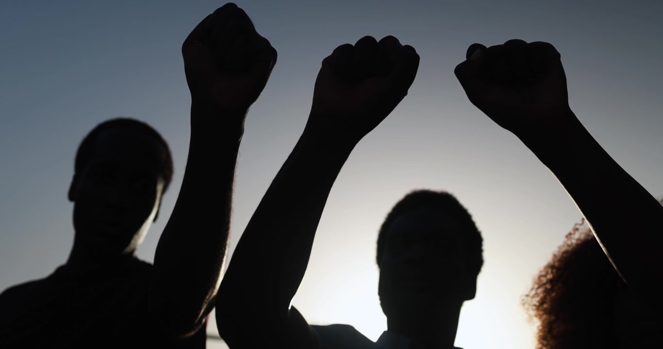 People Raising Fists in Silhouette Against a Bright Sky