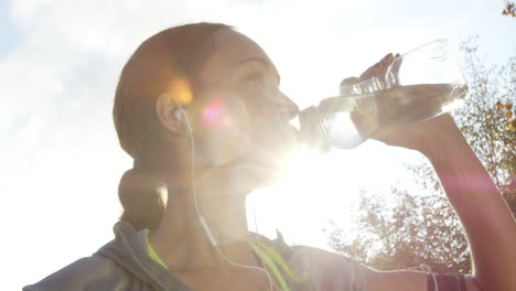 mujer bebiendo agua mientras hace ejercicio al aire libre