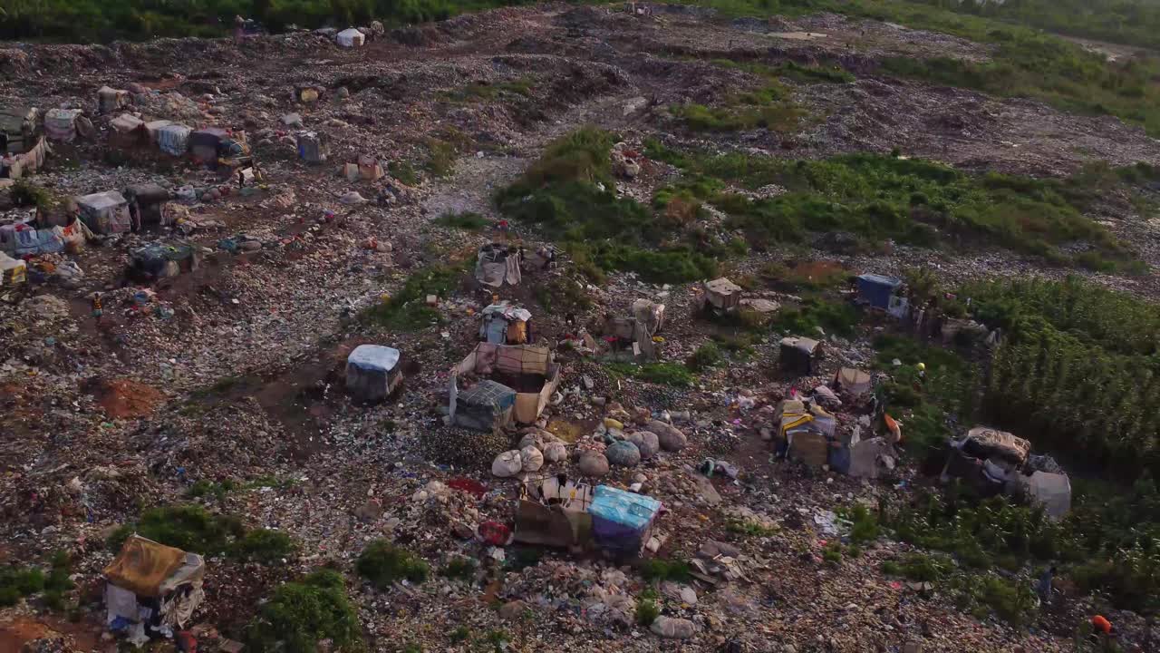Jib up of a large open landfill with garbage pickers walking around in Nigeria, Africa. A display of an average person living in poverty rural area.