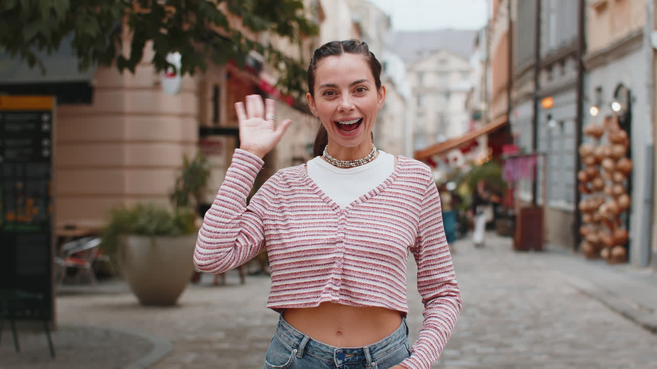 Happy woman smiling friendly at camera waving hands gesturing hello greeting goodbye on city street