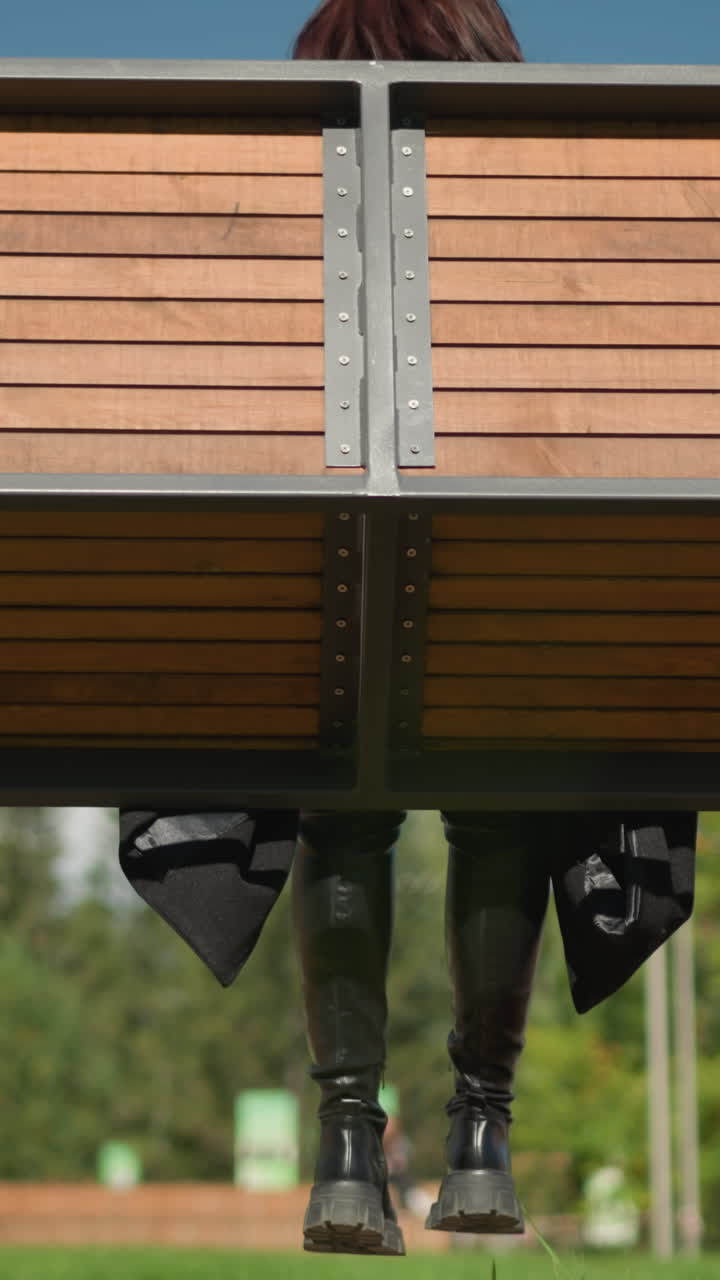 vista trasera de la dama en una silla oscilante de madera balanceándose con el cabello revoloteando en el viento, árboles en el fondo, y figura borrosa moviéndose cerca