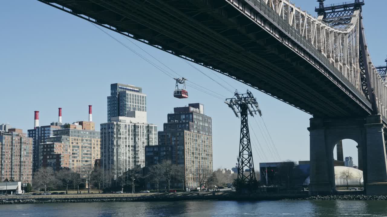 Aerial tram glides under the Queensboro Bridge with Manhattan skyline and East River in view, capturing iconic New York urban life