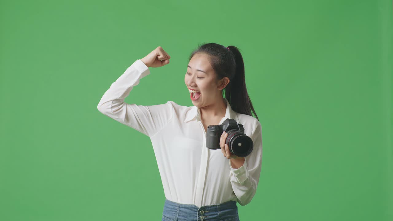 아시아인 사진작가 가 스튜디오 의 초록색 스크린 배경 에 서 있는 동안 손 에 카메라 를 들고 팔꿈치 를 구부린다