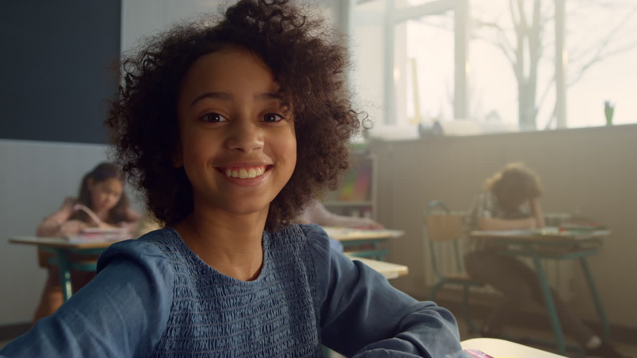 chica africana sentada en el escritorio en el salón de clases. estudiante sonriente posando en la cámara