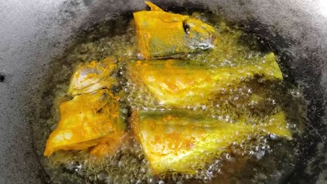 several pieces of fish that have been rubbed with turmeric spices are fried in a pan.