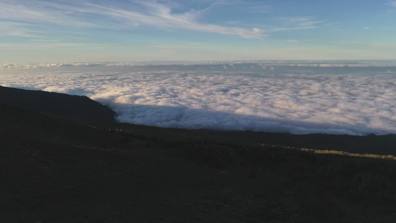 View from a cliff below the Pico de Teide mountain on Canary Islands on a dense cloud inversion in the valley below and the Atlantic ocean on the horizon at sunset. Cloud inversion on a beach 4K.