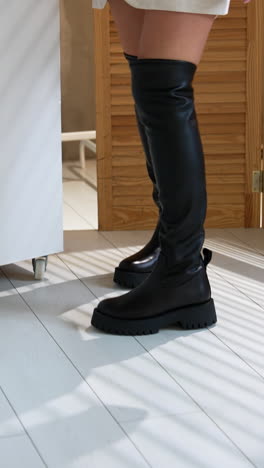 woman turning around in studio demonstrating high black boots on plain tractor soles. lady walks near the white cubes on white floor. vertical video