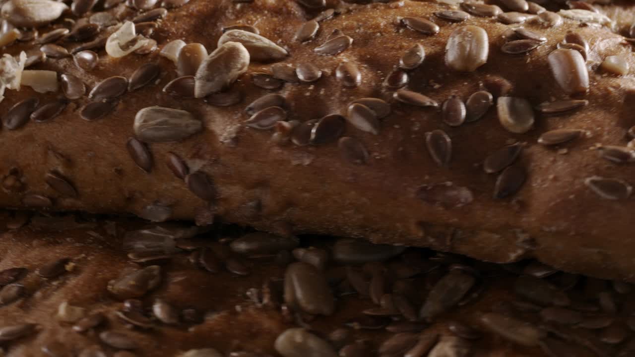 Video di pane rotante con semi di lino e girasole su sfondo nero.