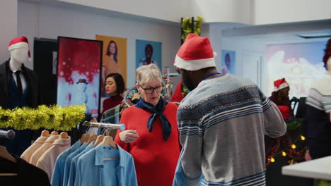 employee assisting older woman with picking right shirt to give as present to husband for upcoming christmas holiday season. client browsing through clothes in xmas adorn fashion shop