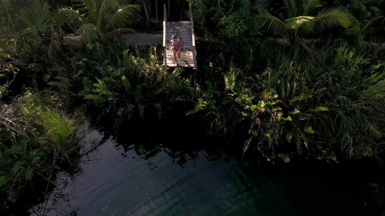 Young woman jumping into cenote (swimming hole) in the jungles of Mexico.