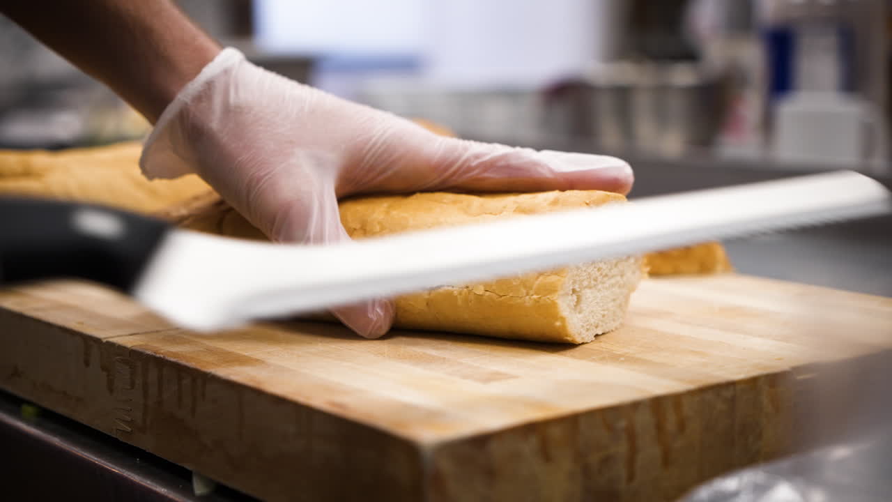 Chef che affetta una baguette di pane francese, primo piano al rallentatore 4K.
