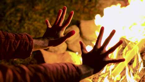 young man warming up his hand at camp fire in a cold night of autumn